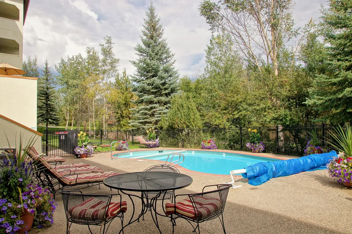 A vibrant outdoor pool area is surrounded by lush greenery, flower pots, and comfortable seating. The pool is inviting for both swimming and lounging, while the adjacent seating area is perfect for outdoor dining or sunbathing.