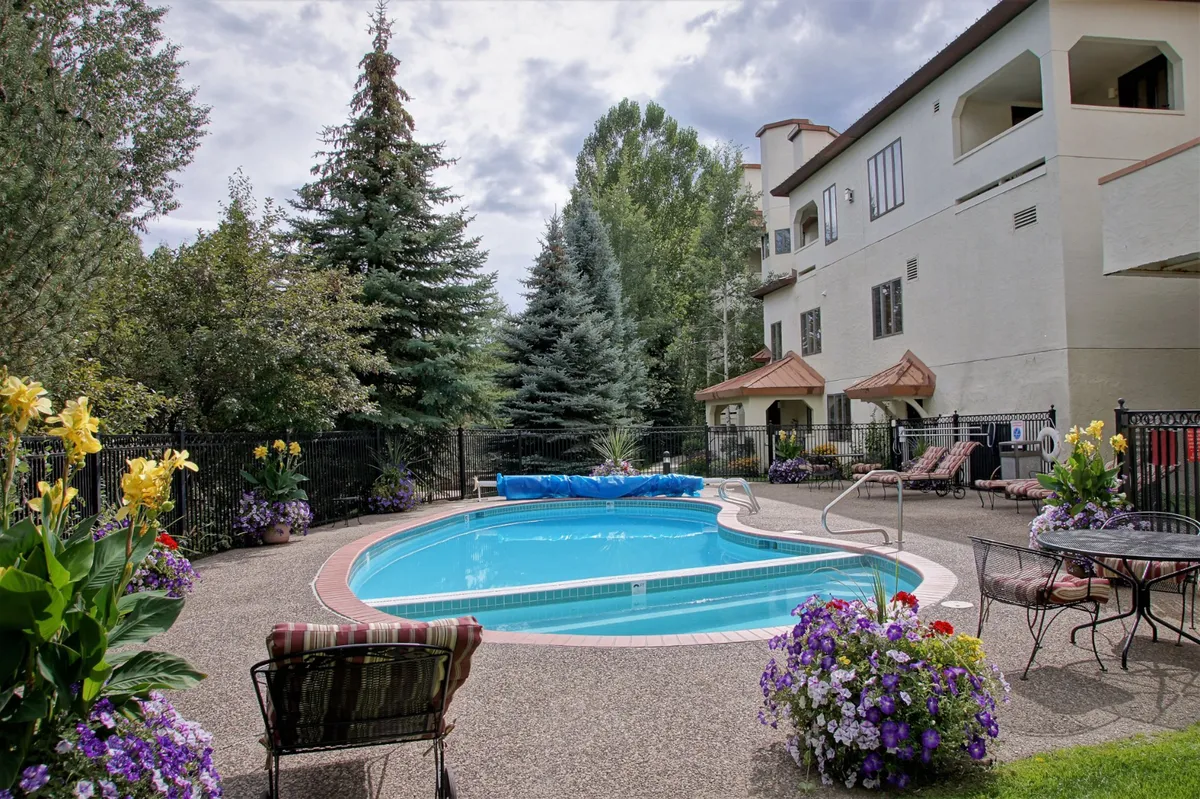 A heart-shaped swimming pool surrounded by lush greenery, colorful flower arrangements, and a comfortable seating area. The atmosphere is tranquil and inviting, ideal for swimming, sunbathing, or relaxing with friends. The pool area is well-maintained and offers a resort-style ambiance that echoes the section's promise of luxury amenities.