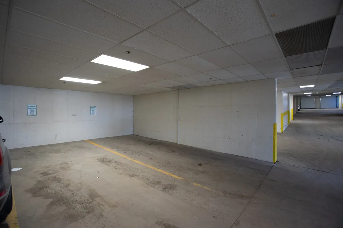 An interior view of the underground parking garage with empty parking spaces, concrete walls, and overhead fluorescent lights. The setting is clean and functional, designed for convenience and comfort in all seasons.