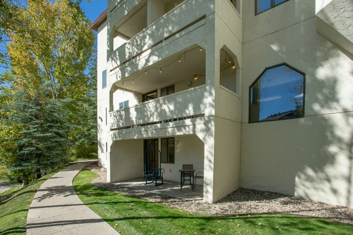 This image presents a welcoming exterior with patio seating, a tree-lined pathway, and the building facade. The scene suggests inviting outdoor spaces ideal for socializing, relaxing, or connecting with nature. The morning sun casts a gentle glow, enhancing the feeling of a tranquil retreat.