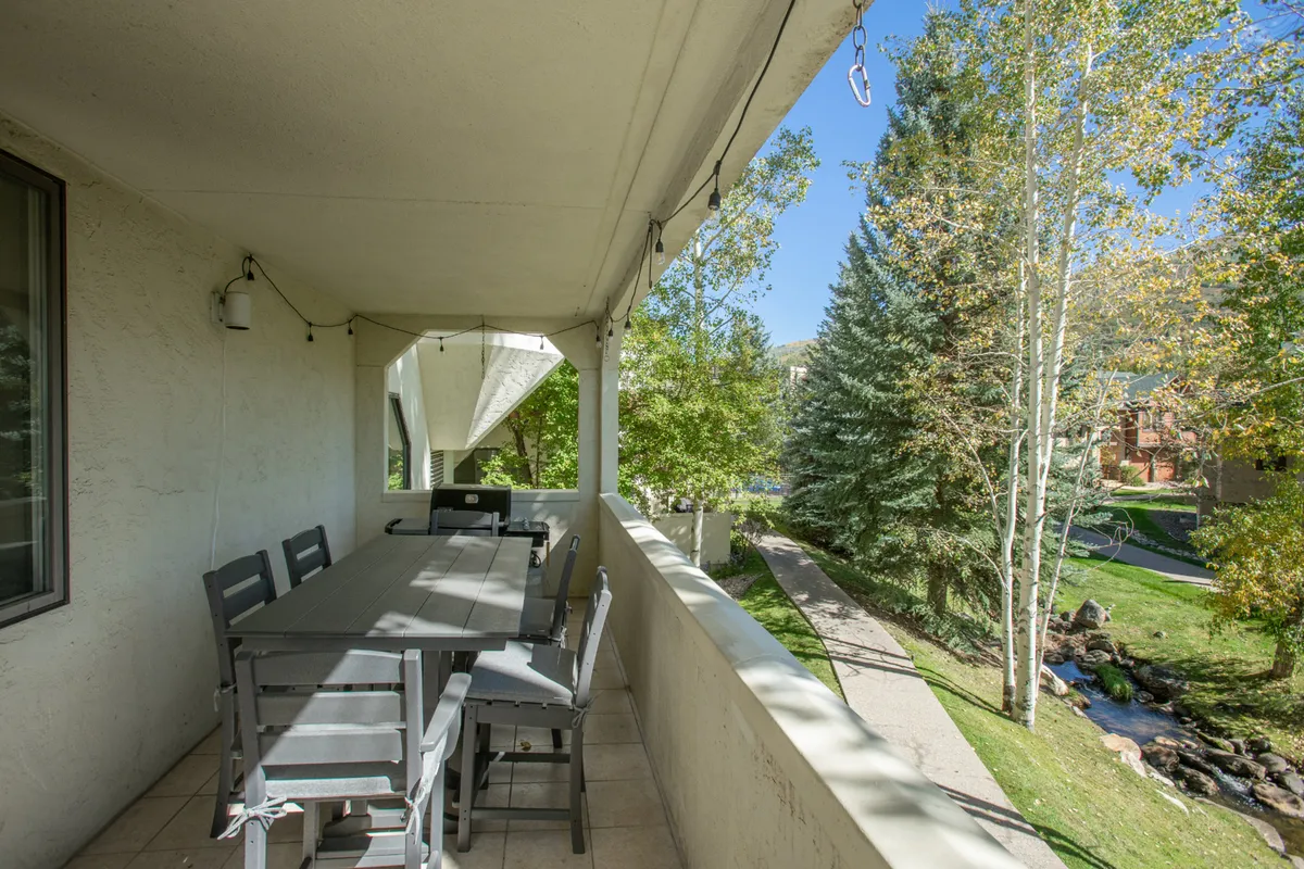 An outdoor dining table set on a tranquil balcony overlooking lush greenery and a stream. The scene is perfect for alfresco dining, with a peaceful atmosphere that invites guests to enjoy morning coffee or sunset dinners surrounded by nature.
