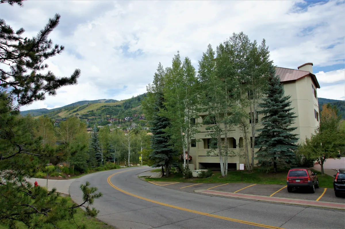 An exterior image showing the building surrounded by tall trees, with mountains looming in the background. The setting is calm and inviting, showcasing the property's integration into the natural landscape and proximity to outdoor adventure.