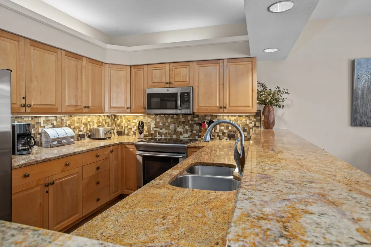 A modern kitchen with granite countertops, stainless steel appliances, wooden cabinets, and a decorative backsplash. The inviting bar-height counter is set for casual coffees or après-ski snacks, and the layout is ideal for socializing or meal prep.