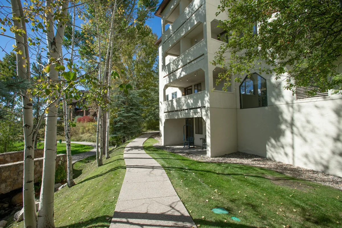 The image shows the building’s balconies overlooking a winding path among mature trees. The scene conveys opportunities for morning coffee outdoors, peaceful strolls, and immediate access to nature from the property itself.