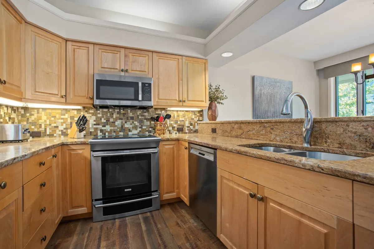 A bright kitchen scene with granite countertops, stainless steel appliances, and detailed tile backsplash. The inviting space provides plenty of room for meal prep and gathering.