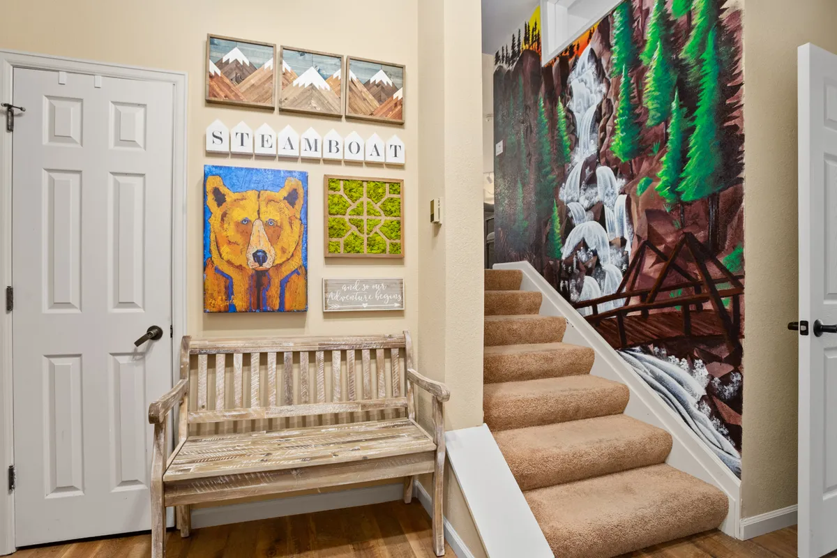 A welcoming entryway featuring a decorative bench set against a backdrop of mountain-inspired art, including a bear painting and waterfall mural. The space is bright and designed for greeting guests or preparing to head out for adventure.