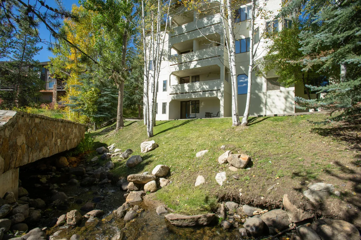 This exterior view shows the building nestled among greenery, with Burgess Creek running alongside. A balcony juts over the creek, illustrating the private outdoor spaces where guests can unwind and connect with nature.
