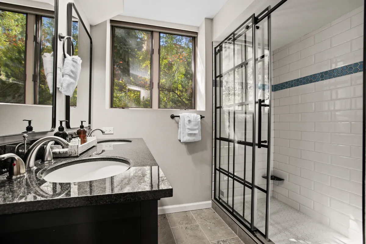 A spacious bathroom with double sinks atop a granite countertop, a large glass shower, and wide windows that fill the room with light. The design is sophisticated yet inviting, ideal for prepping for daily adventures or winding down in the evening.