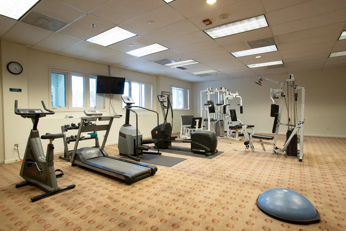 A spacious, well-equipped fitness center with treadmills, elliptical machines, weight training equipment, and exercise balls. The area is bright and motivational, designed for both cardio and strength training. The modern machines and open layout make it ideal for morning workouts as described in the section.