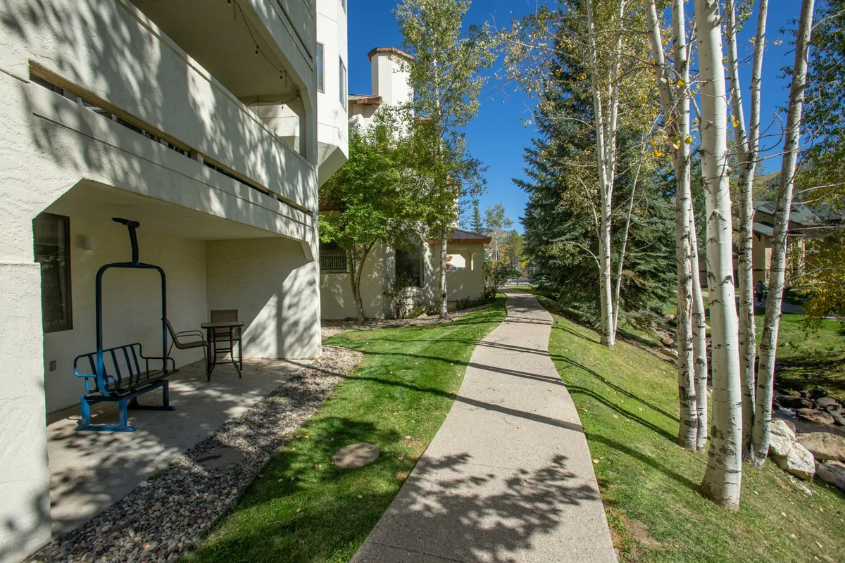 A serene outdoor scene depicting a pathway and outdoor seating area nestled among trees. The image conveys an inviting atmosphere for morning strolls, afternoon relaxation, or gathering before heading out for mountain adventures.