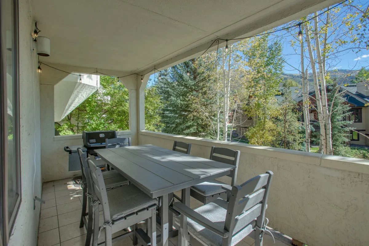 An outdoor dining table set among tall trees, accompanied by a barbecue grill. The space is surrounded by nature, creating a relaxed atmosphere ideal for sunset dinners, morning coffee, or weekend brunches. The setting evokes the creekside picnic area referenced in the section.